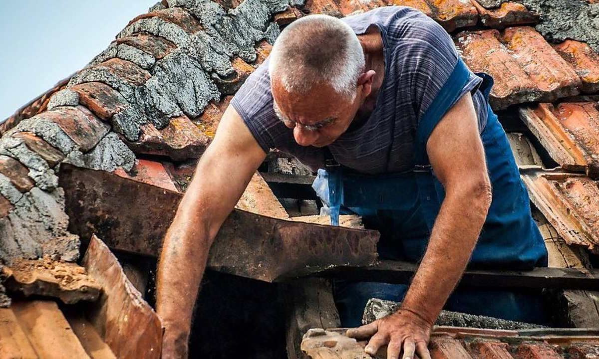 Operario levantando tejas viejas para revisar el soporte de madera de una cubierta