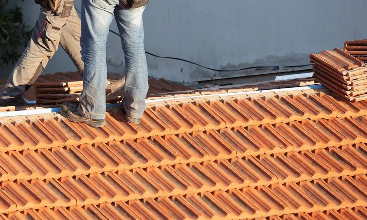 Dos operarios caminando sobre un faldón de teja nueva en un día seco