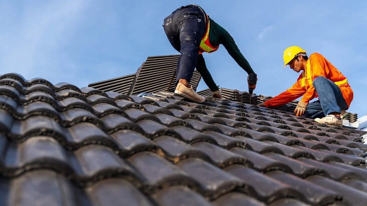 Dos tejadores atornillando teja sobre la cubierta de una vivienda en Lugo