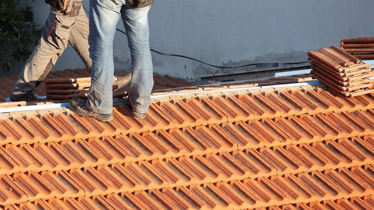 Tejadores retejando una cubierta con teja del país apilada sobre el faldón en Lugo