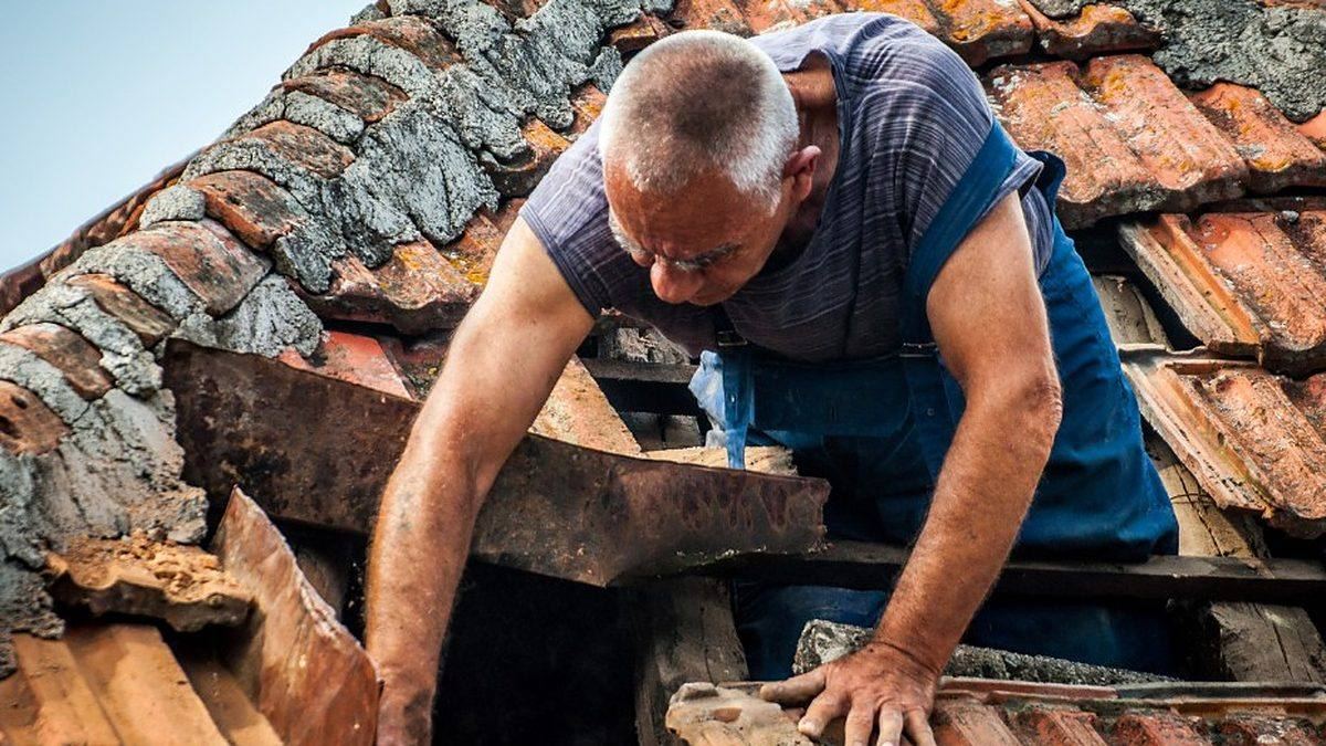 Tejador retirando teja del país partida en el retejado de una casa de piedra de Outeiro de Rei